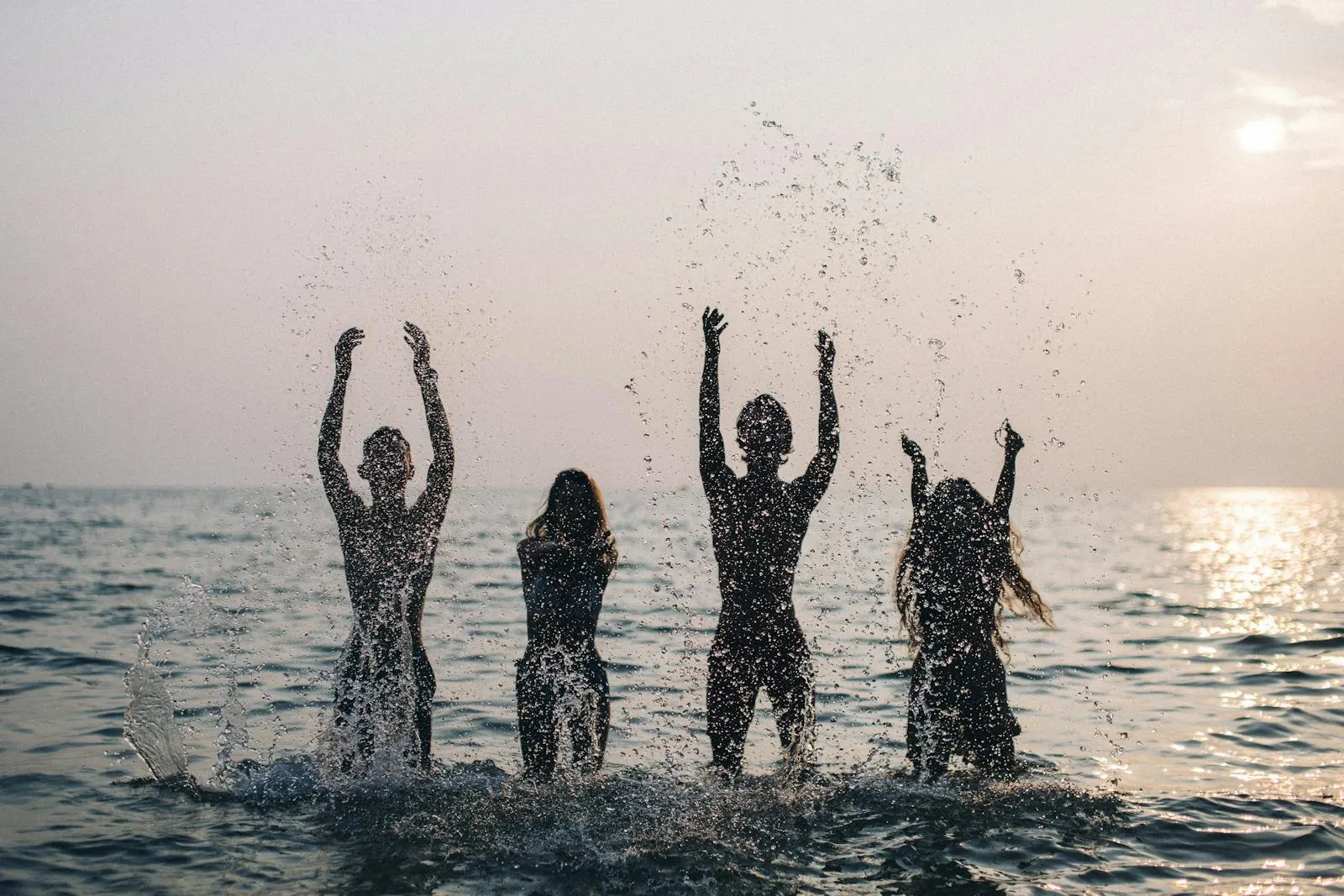 Silhouettes of people playing in the sea at sunset in Favignana, among backlit splashes of water